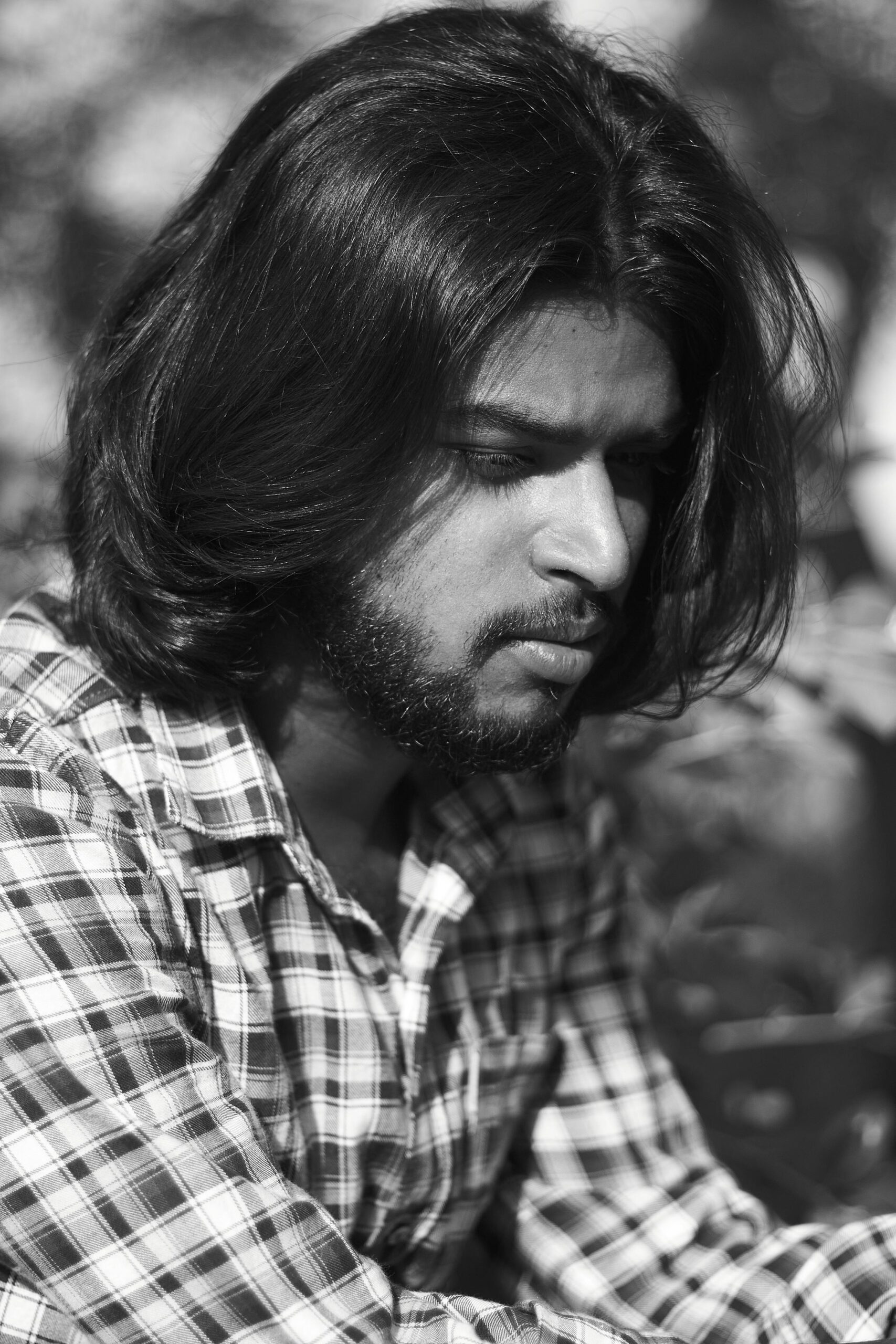 Black and white portrait of a bearded man lost in thought outdoors.