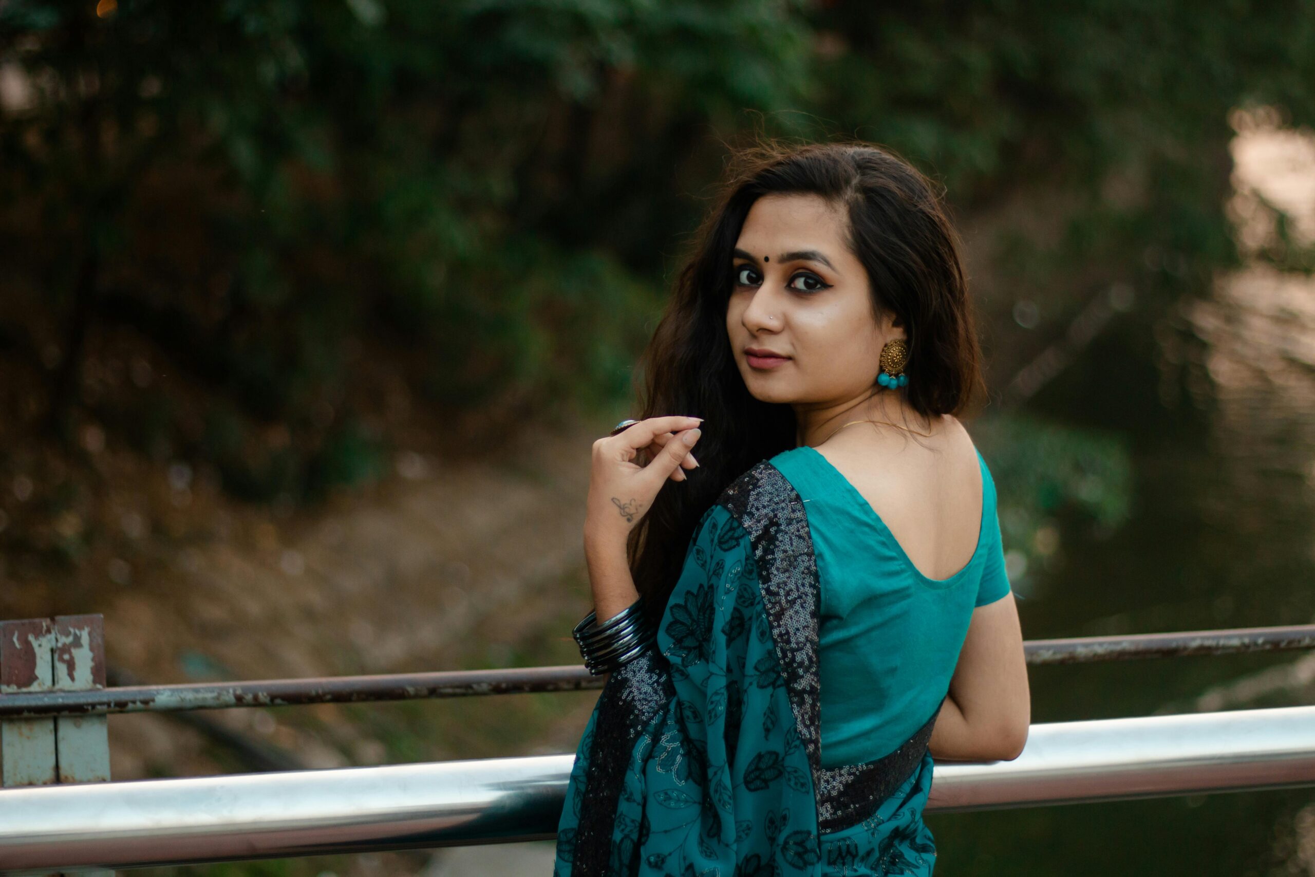 Portrait of a woman in teal sari looking over her shoulder outdoors.